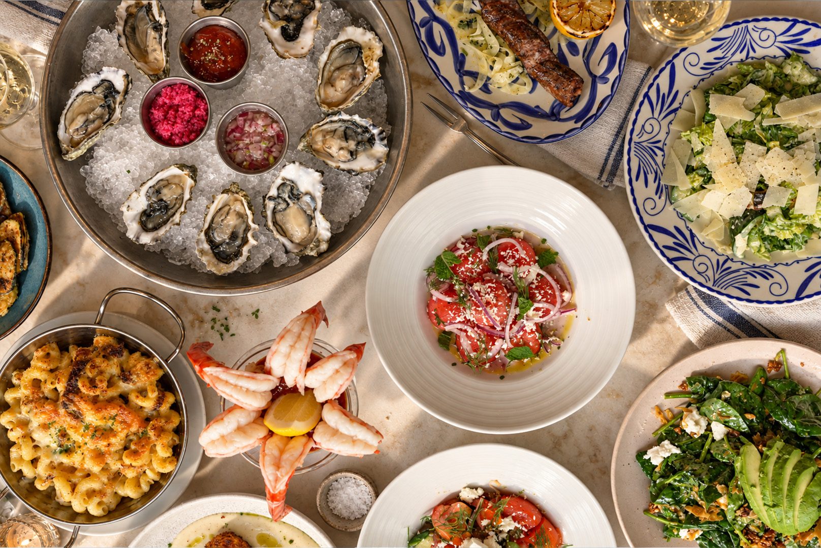 Oysters, salads, shrimp cocktail and mac and cheese spread across a table at Nisi Greek Grill